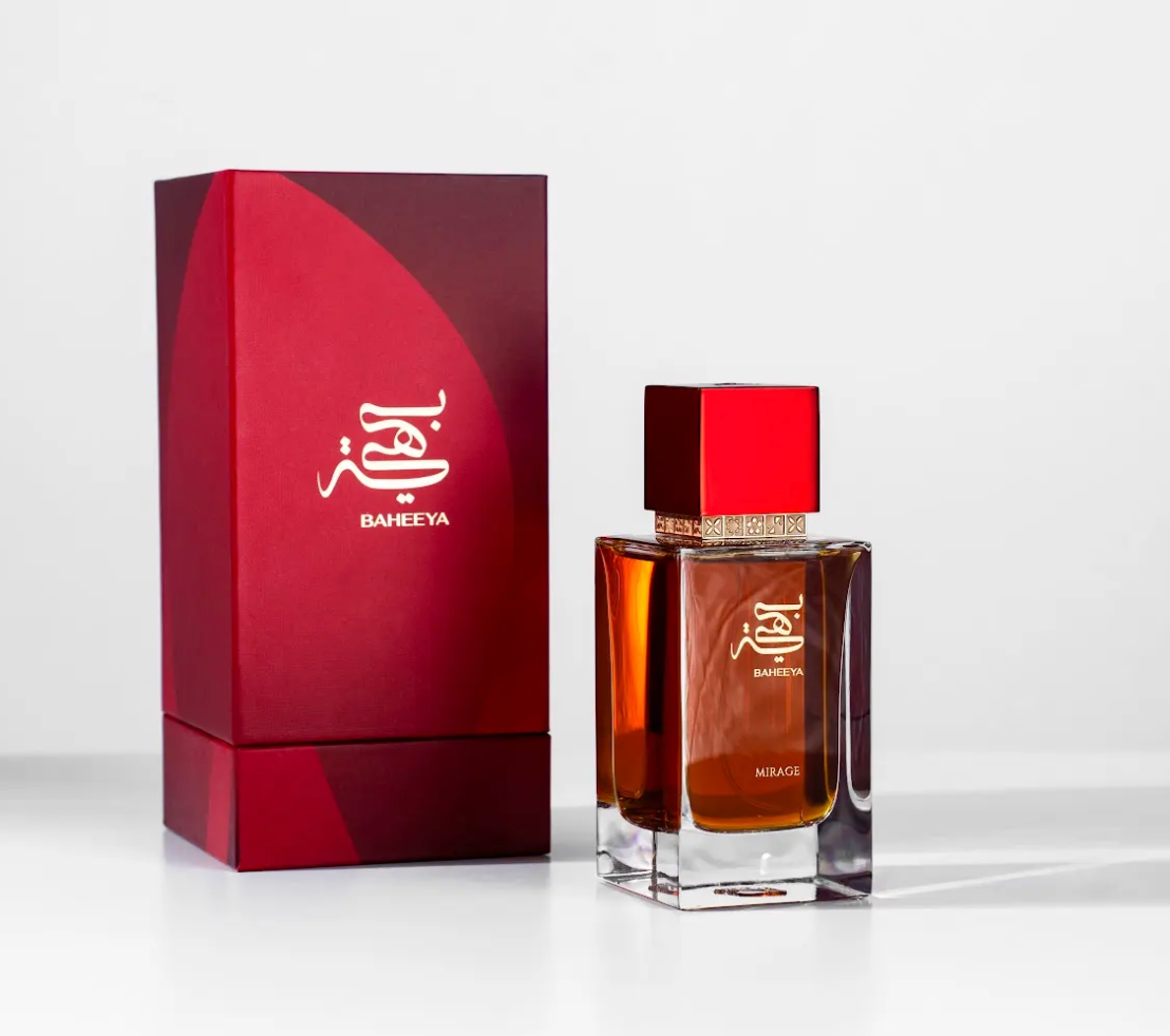 A bottle of Baheeya perfume with amber liquid and a red cap stands next to its matching red box on a clean white background.