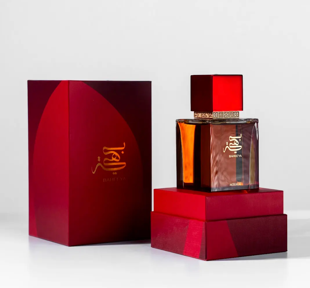 A luxury perfume bottle with a square amber-brown glass body and a glossy red cap, displayed next to its matching deep red presentation box on a clean white background.