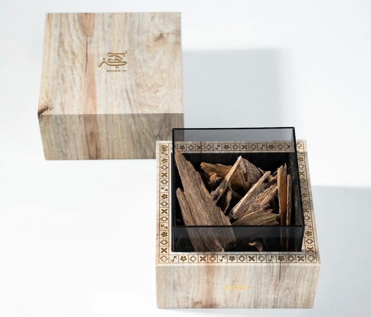 Wooden box with decorative lid containing oud wood sticks on a white background